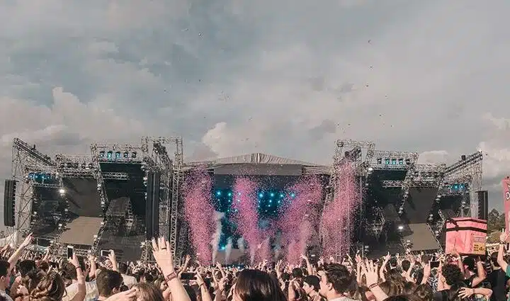 Um placo montado com luzes azuis e fumaça rosa com muitas pessoas pulando na frente