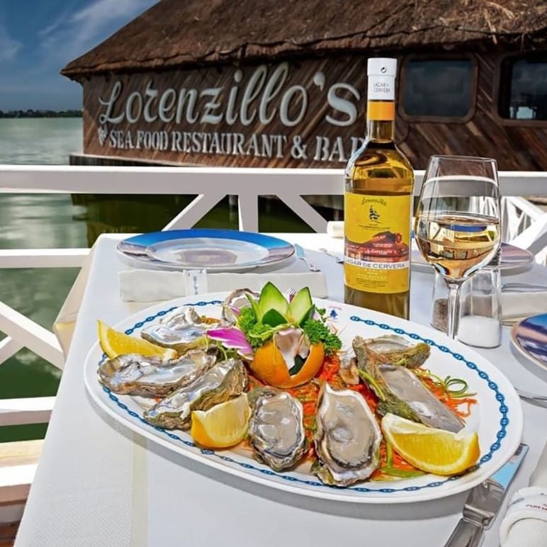 Prato de ostras com limão e uma taça ao lado de uma garrafa ao fundo. Atrás pode-se ver o restaurante Lorenzillo's, recomendação em Cancún