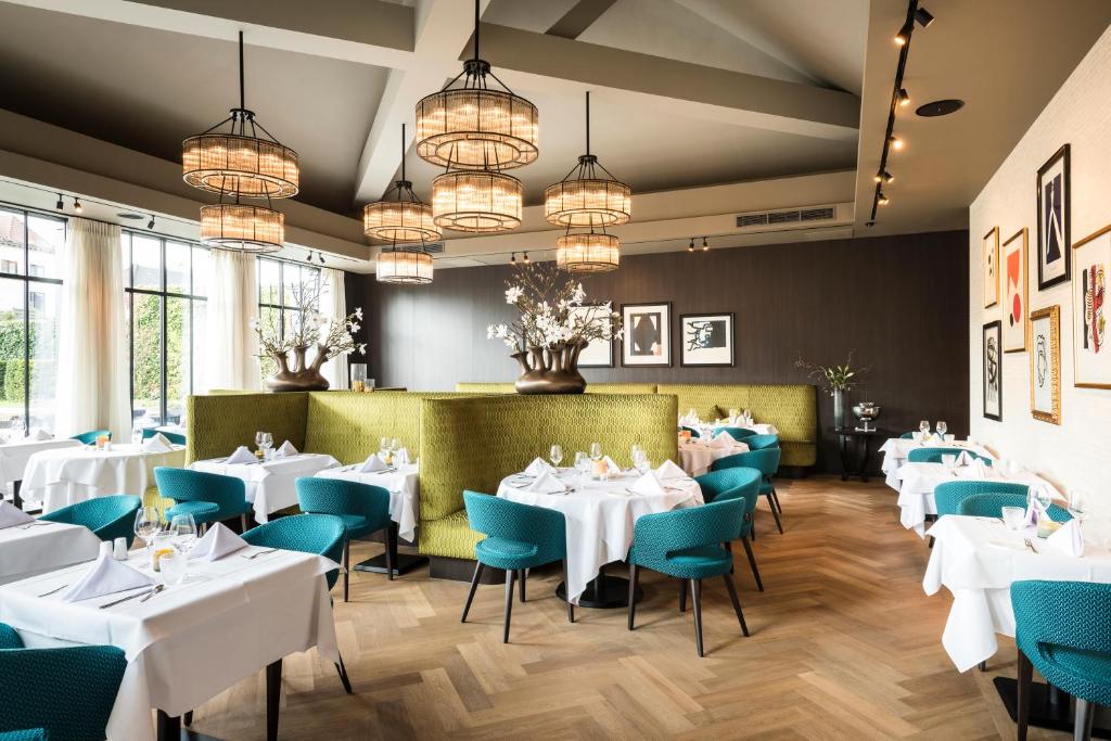 lounge do restaurante do Dukes' Palace Brugge, um dos hotéis em Bruges, com mesas de toalha branca e cadeiras acolchoadas verdes, lustres no teto e porta de vidro
