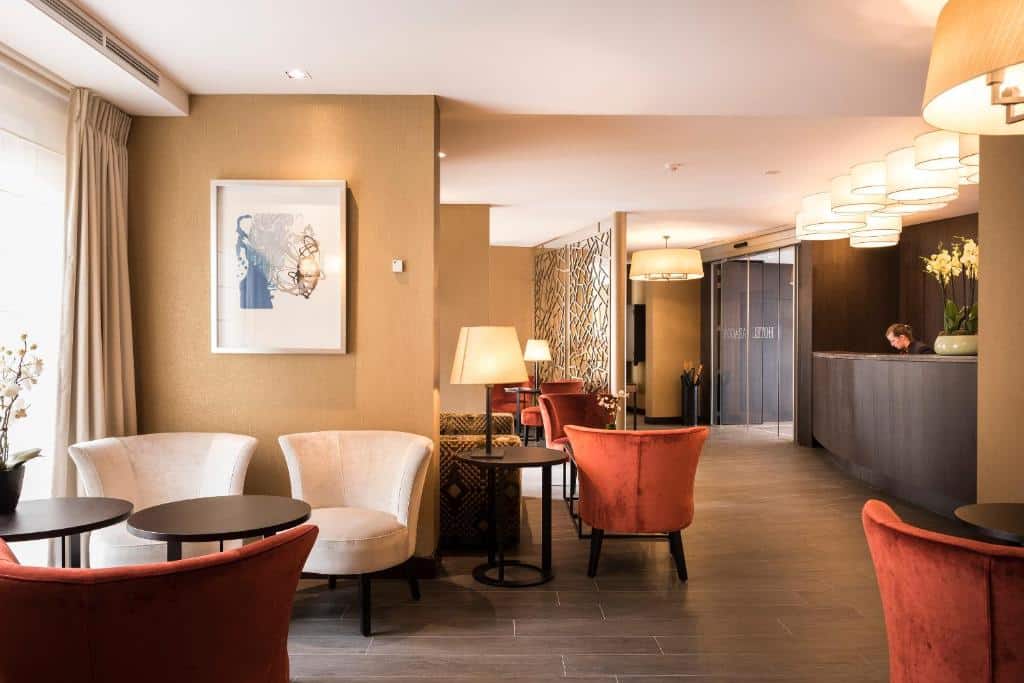 lounge com recepção e quadros nas paredes amareladas com poltronas brancas e laranjas e mesas de madeira no Hotel Aragon, um dos hotéis em Bruges