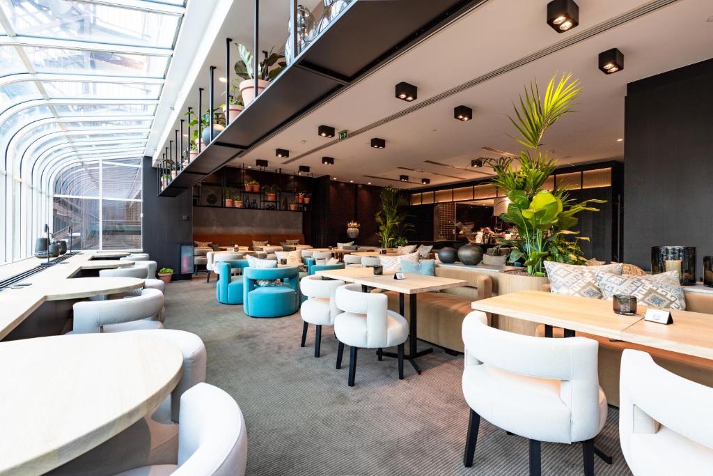 lounge em dois andares do The Hotel Brussels, um dos hotéis em Bruxelas, com diversas mesas em cor de madeira e poltronas brancas em decoração sofisticada