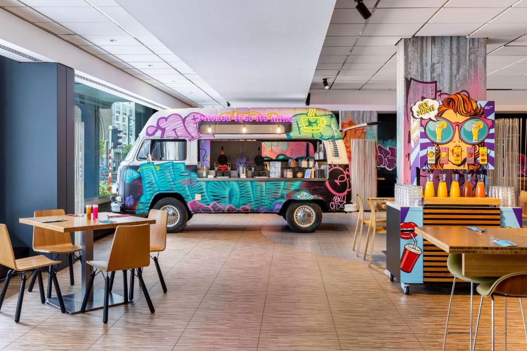 lounge amplo do nhow Brussels Bloom, um dos hotéis em Bruxelas, com mesa e cadeiras, uma estação de sucos e uma mini kombi adaptada como estação de comidas, tudo decorado com grafites em tons de azul e rosa em sua maioria