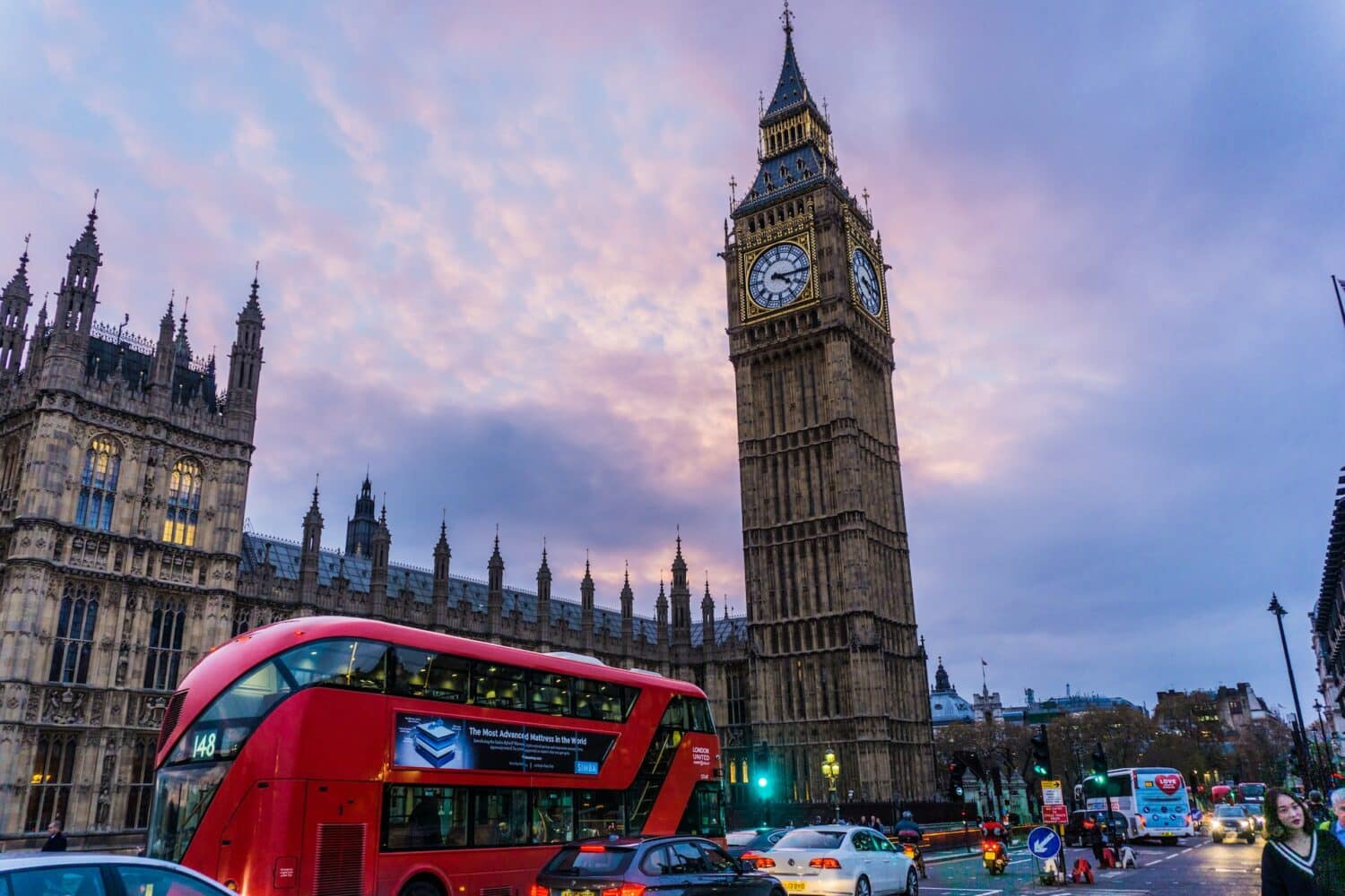 Rua movimentada em Londres com um dos icônicos ônibus vermelho passando, e ao fundo, dá para ver a torre do Big Ben