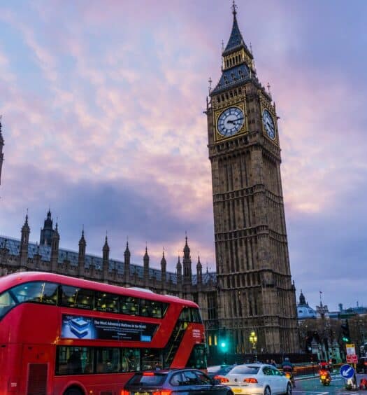 Rua movimentada em Londres com um dos icônicos ônibus vermelho passando, e ao fundo, dá para ver a torre do Big Ben