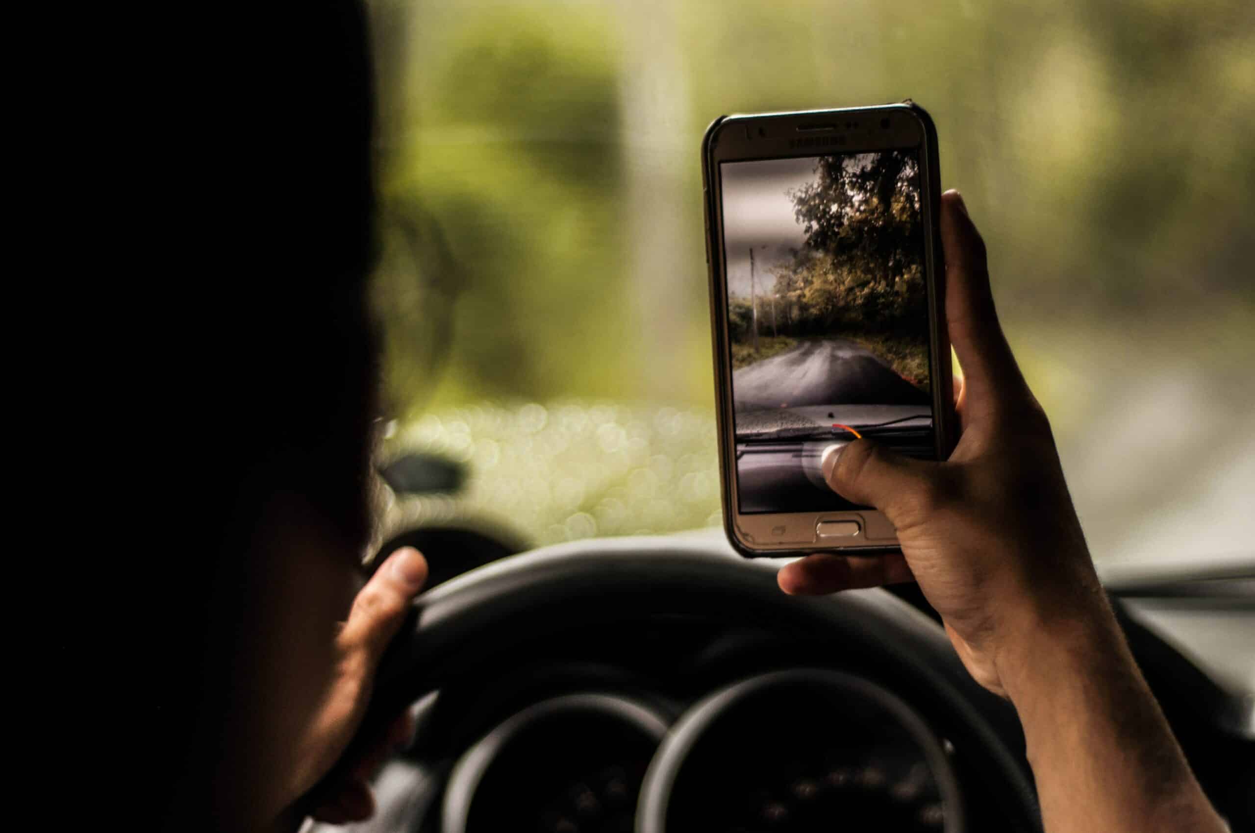 homem dirigindo e segurando um celular android enquanto grava um vídeo da estrada, úmida de chuva e com belas árvores ao longo do asfalto