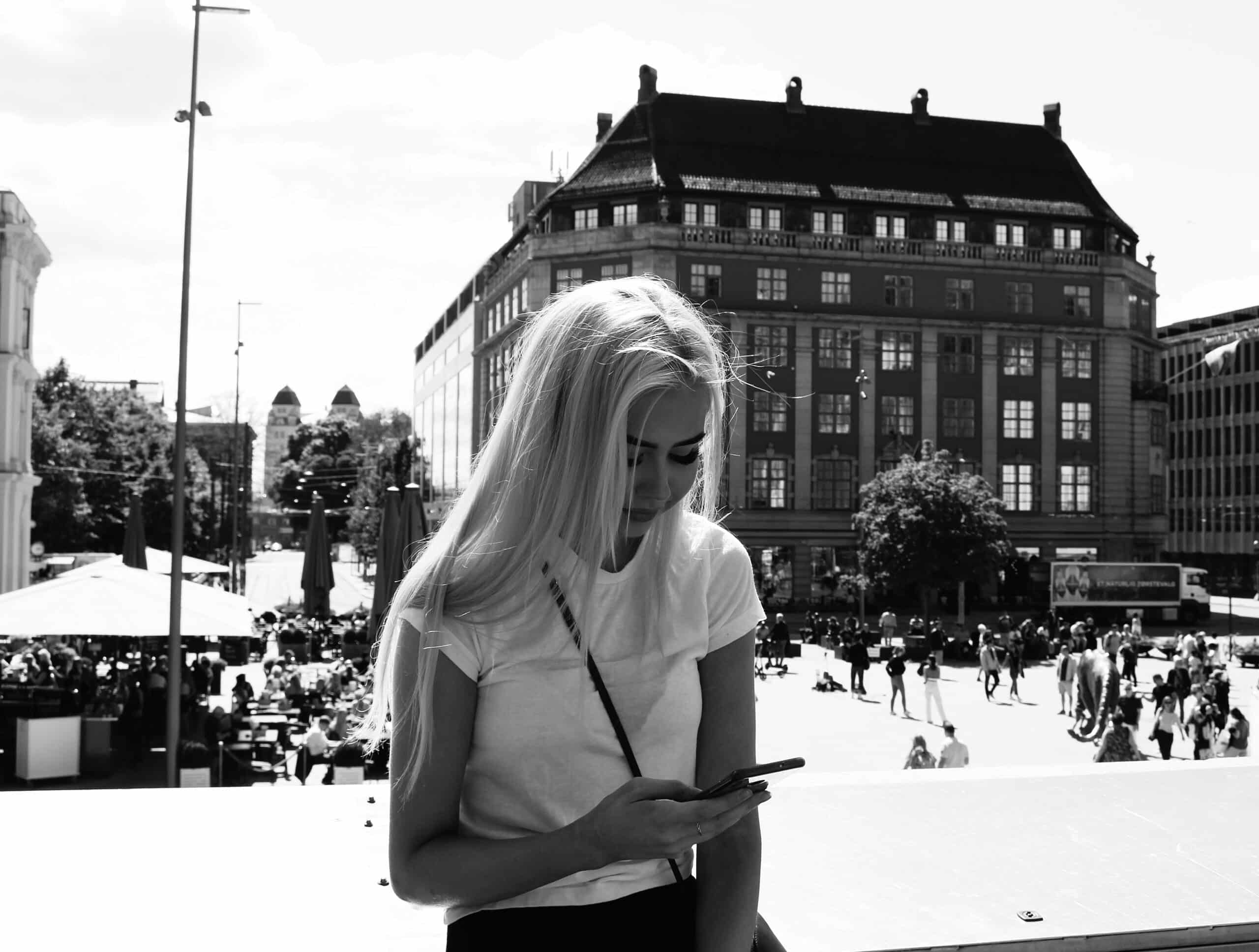 Menina loira com celular na mão na Estação central de Oslo, imagem preto e branco. Representa chip celular Oslo