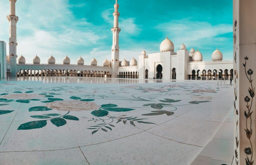 Pátio com ilustração de rosas e uma mesquita branca com céu azul ao fundo para ilustrar o post de chip de celular para os Emirados Árabes. - Foto: Mohammed Bukar via Unsplash