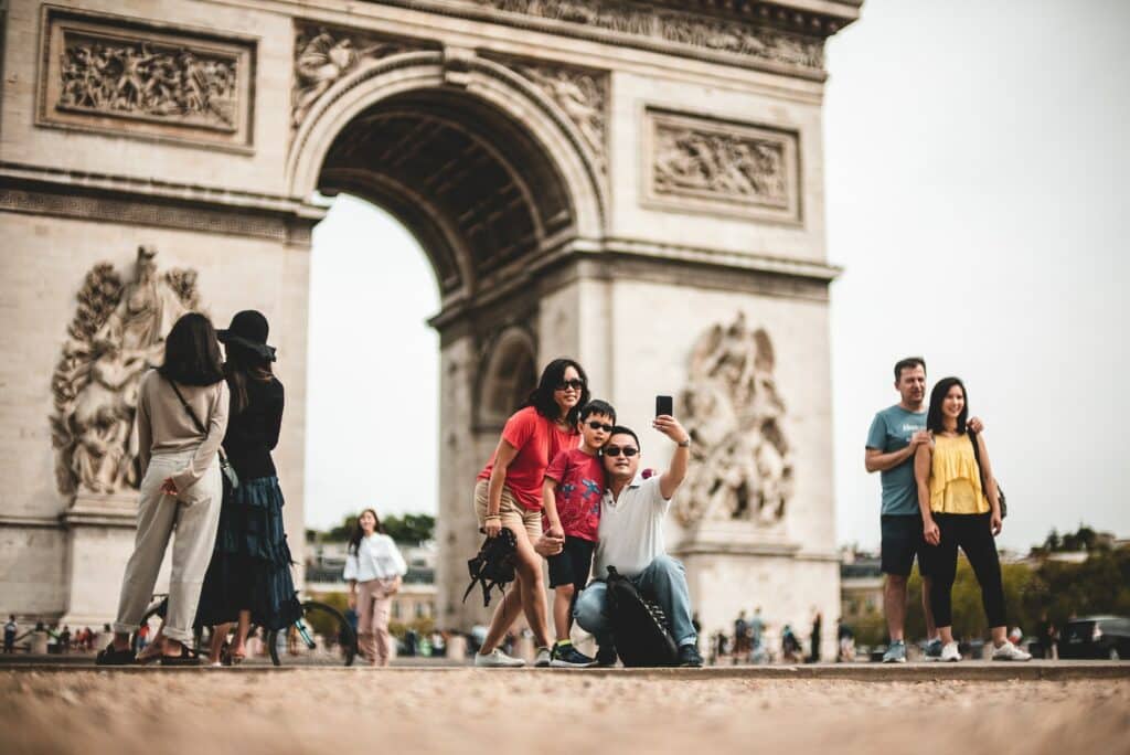 Uma família, com uma homem, um menino e uma mulher, juntos em frente ao Arco do Triunfo, construção histórica de Paris em formato de arco, tirando uma selfie juntos