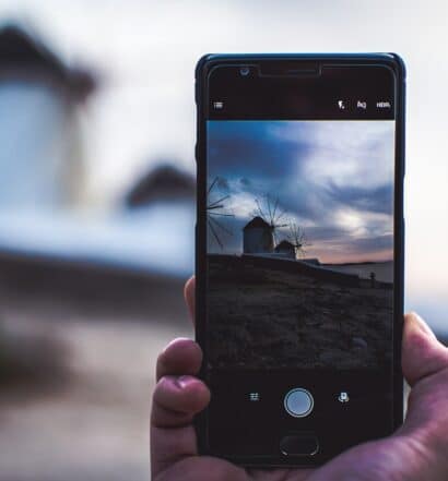 Uma mão segurando o celular, com a câmera ligada, mostrando a imagem dos moinhos de vento de Mykonos num fim de tarde