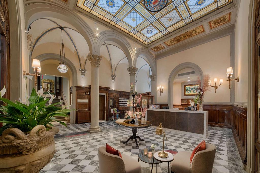Recepção do NH Collection Firenze Porta Rossa, um dos hotéis na Toscana, com decoração clássica, mesa com flores, poltronas com mesinha redonda ao meio, e escada que dá acesso aos outros comodos do hotel