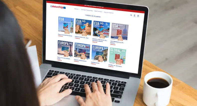 mulher digitando no computador em cima de uma mesa de madeira com uma xícara branca ao lado cheia de café. Na tela do computador é possível ver a página do site o meu chip