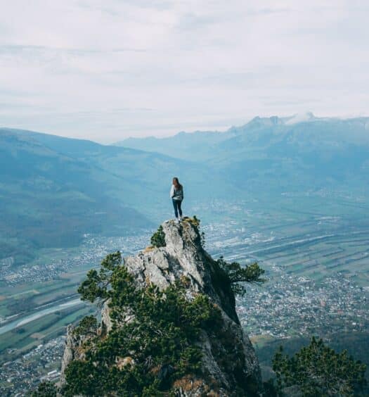 Mulher no topo de uma montanha olhando para a cidade em frente. - Foto: Oliver Schwendener via Unsplash