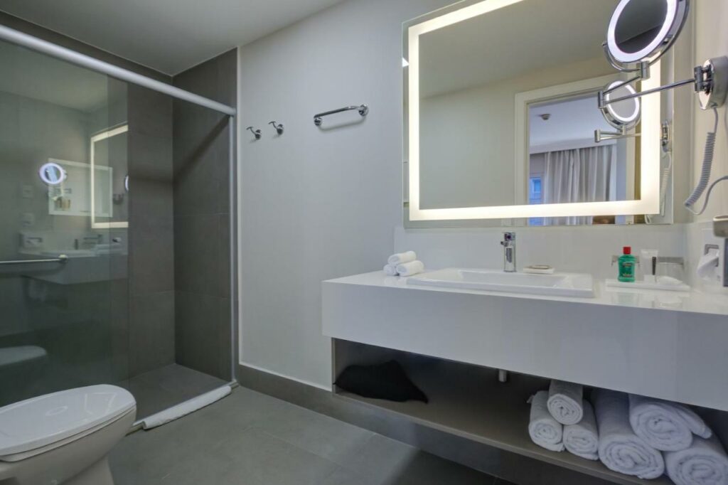 Banheiro grande do Park Inn by Radisson Berrini com um box com barras de apoio, pia mais baixa e um amplo espelho
