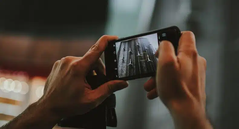 Uma pessoa segura um smartphone na horizontal para tirar uma foto em close de uma superfície de madeira desgastada.