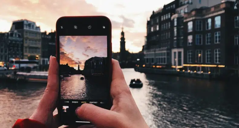 Pessoa branca tirando foto de torre de igreja e canal ao final da tarde. - Foto: Max Kukurudziak via Unsplash