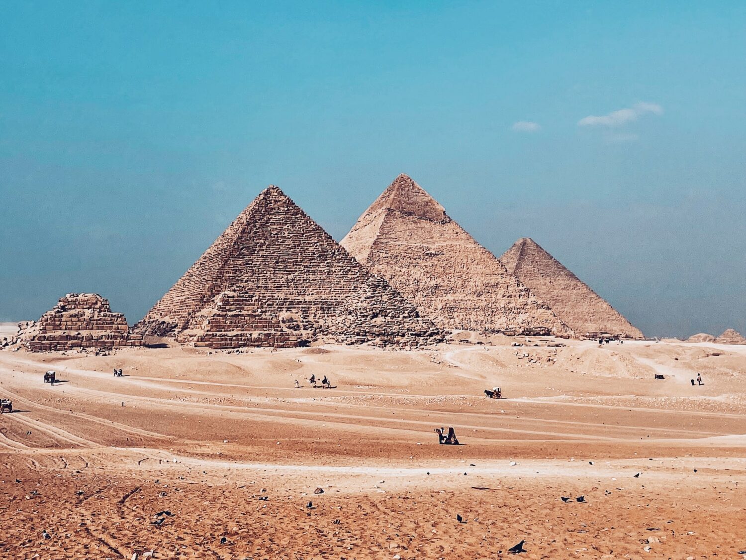 as três Pirâmides de Gizé, no Egito, em diferentes tamanho em meio ao deserto em tons de amarelo e alaranjado e ceu azul