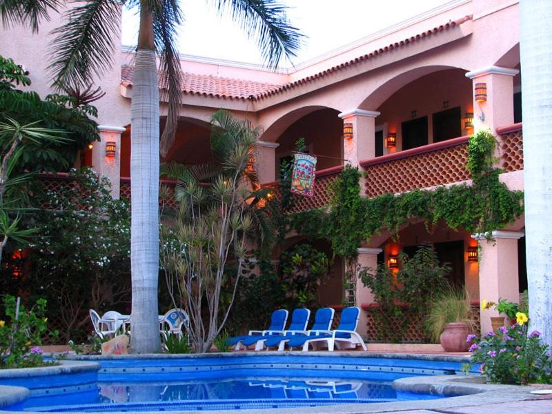 Piscina do Los Barriles Hotel com cadeiras em volta. A arquitetura do local é rustica em tons de rosa, com plantas em volta. Representa hotéis em Los Cabos.