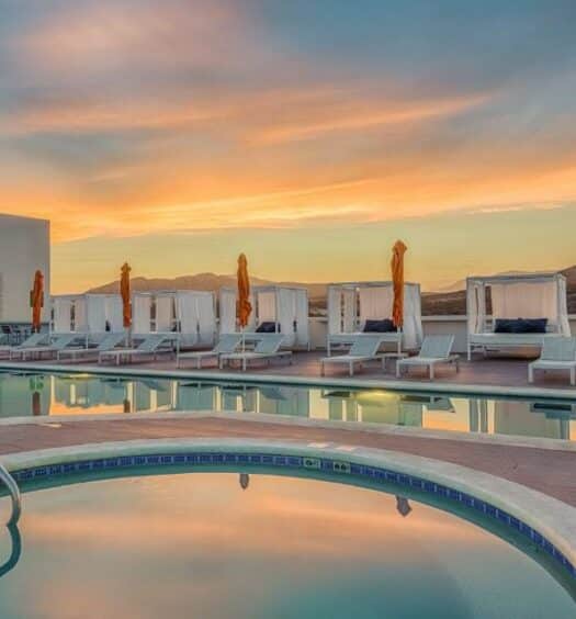 Vista da piscina do Hampton Inn & Suites by Hilton Los Cabos no pôr-do-sol com cadeiras em volta. Representa hotéis em Los Cabos
