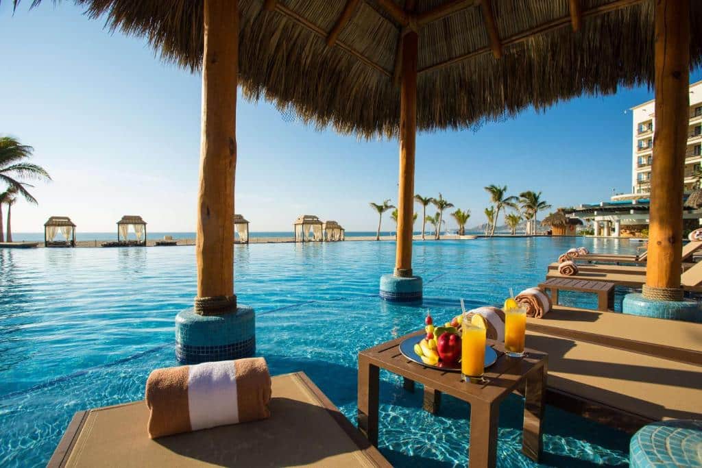Vista da piscina do Hyatt Ziva Los Cabos – All Inclusive com cadeiras dentro da água e com vista para o mar e céu azul. Representa hotéis em Los Cabos.