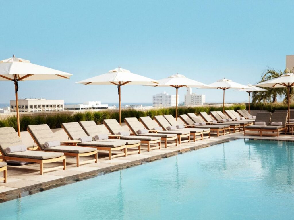 Piscina do Santa Monica Proper Hotel, a Member of Design Hotels, ao redor há um deck pequeno com espreguiçadeiras cinzas com almofadas ao redor da piscina, além de guarda-sóis brancos
