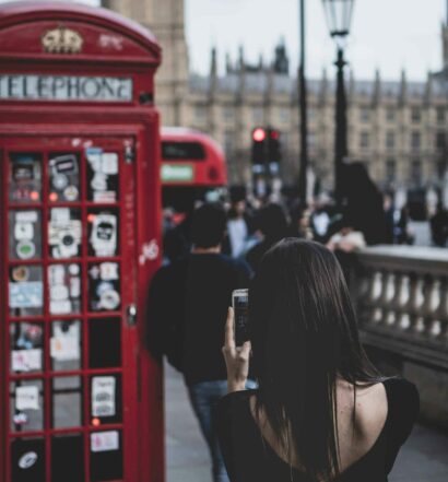 pessoa segurando um celular batendo uma foto de outra encostada em uma cabine telefônica vermelha em Londres com vista para a Praça do Parlamento e o Big Ben de fundo, ilustrando o post de chip celular Londres