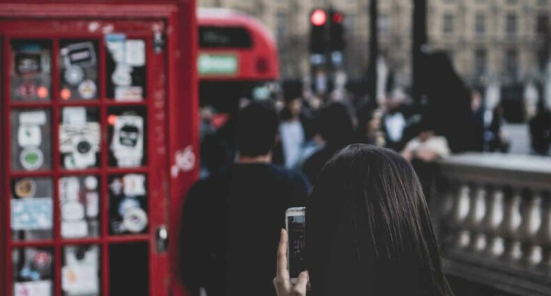 pessoa segurando um celular batendo uma foto de outra encostada em uma cabine telefônica vermelha em Londres com vista para a Praça do Parlamento e o Big Ben de fundo, ilustrando o post de chip celular Londres