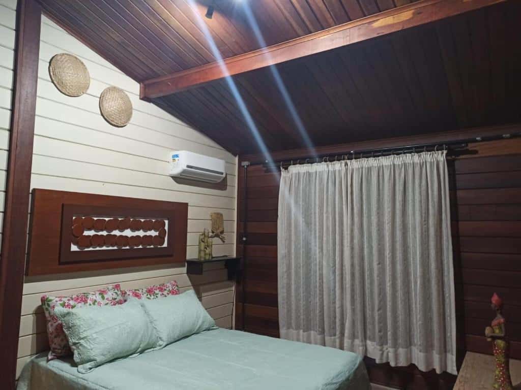 quarto com cama de casal, cortina na janela, detalhes em madeira e ar-condicionado na Belas Águas Mairiporã