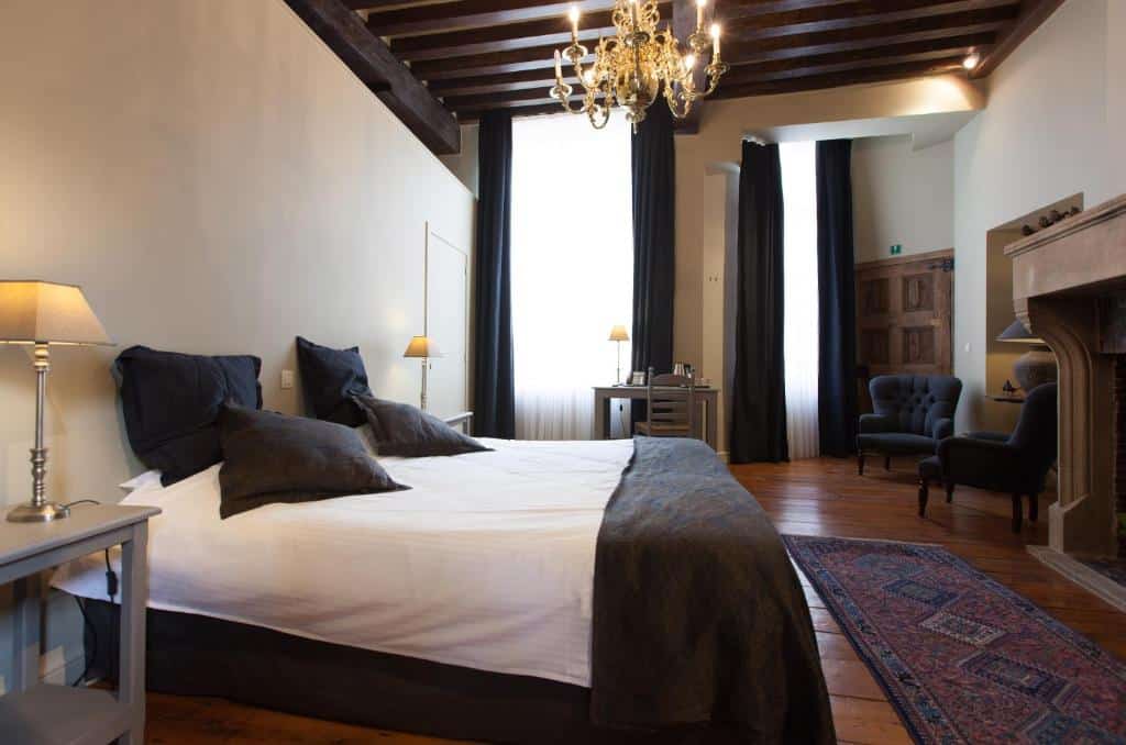 quarto do Hotel Boterhuis, um dos hotéis em Bruges, com cama grande, janela enorme pegando grande parte da parede, há luminárias dos lados da cama e uma mesa com cadeiras de um lado e poltronas do outro, na frente da cama, uma lareira