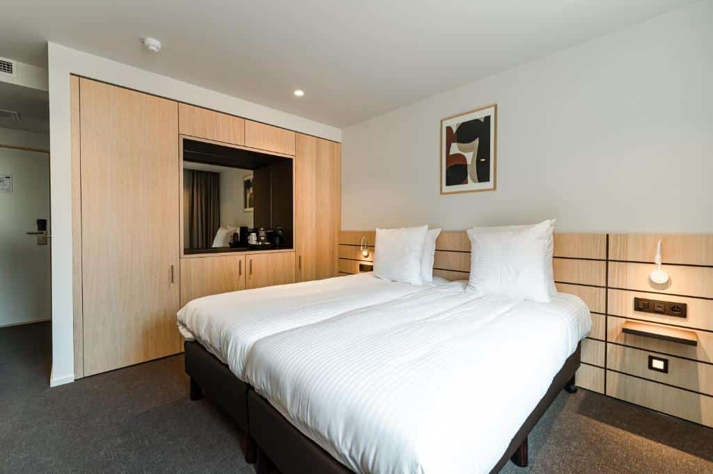 quarto do Hotel Le Bois De Bruges com duas camas unidas para formar um cama maior, ao lado, um guarda-roupa grande de madeira com espelho e do outro, uma mesinha de cabeceira
