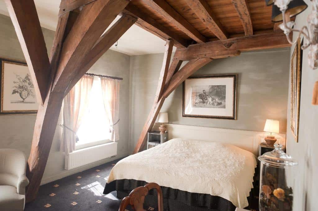 quarto com uma estrutura de madeira do teto aparente com cama de casal, janela com cortina e mesinha com quadro na parede no Hotel Ter Brughe