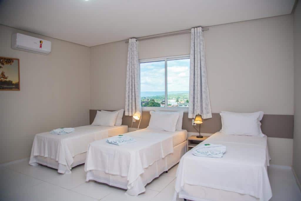 três camas de solteiro, luminárias, janela com vista e ar-condicionado na Hotel e Pousada Flor do Juá