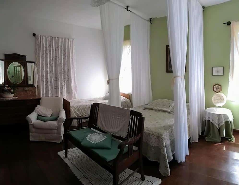 quarto com dossel branco, sofá em estilo rústico com detalhes esverdeados na Refúgio Pasárgada Guest House