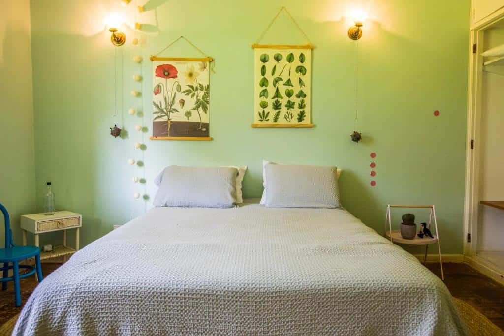 quarto com cama de casal e luminárias dos dois lados, parede verde com posters que mostram natureza e flores no Villaggio Serra da Cantareira