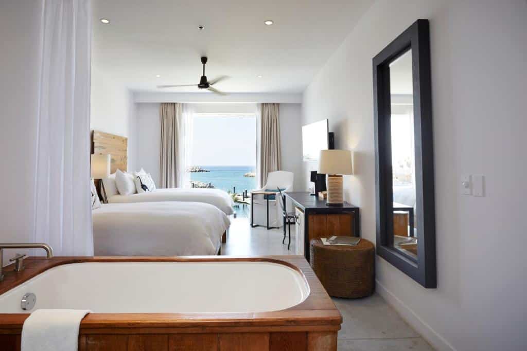 Quarto do Hotel El Ganzo Adults Only com banheira de hidromassagem, duas camas de solteiro, TV em frente a cama com mesa de trabalho e sacada com vista para o mar.