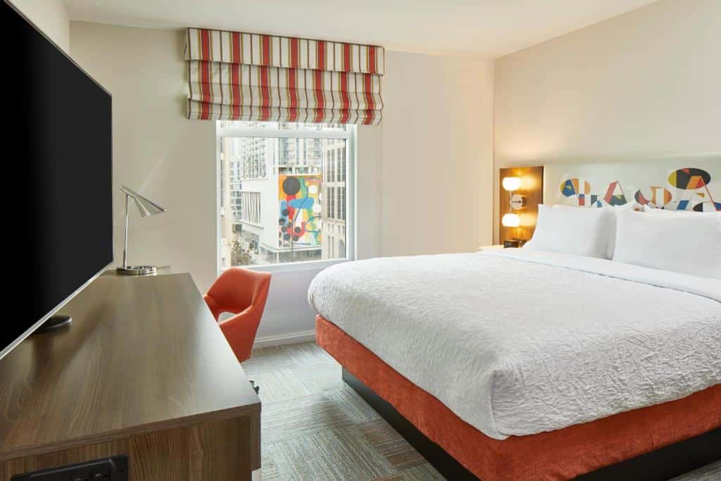 Quarto do Hampton Inn & Suites Atlanta-Midtown, Ga com cama de casal, luminária ao lado esquerdo em cima da cômoda. Tv em frente a cama e mesa de trabalho ao lado da janela do lado esquerdo.