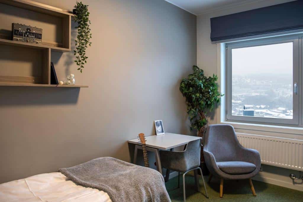 Vista do quarto Oslo Hostel Rønningen com cama de solteiro, mesa de trabalho e poltrona cinza perto da janela.