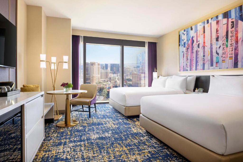 Quarto do Las Vegas Hilton At Resorts World com uma janela panorâmica com vista para a cidade, o carpete desenhado com azul e amarelo, duas camas de casal, e de frente para as camas há uma cômoda com gavetas com uma televisão sob ela, para representar os resorts em Las Vegas