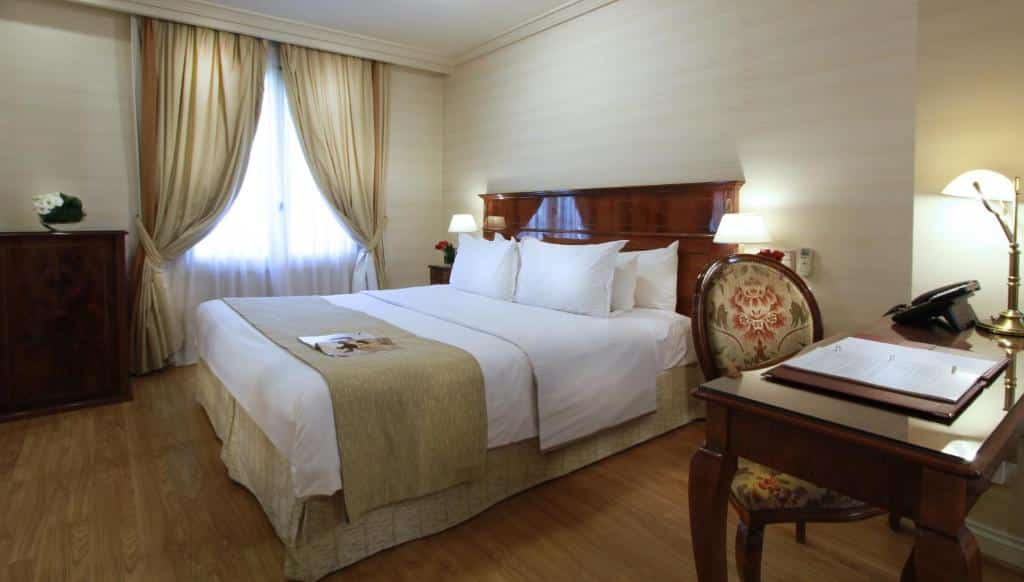 Quarto do Melia Recoleta Plaza Hotel com uma cama de casal, uma mesa de escritório com uma cadeira, uma janela com cortinas e uma cômoda, tudo em madeira e roupas de cama em bege e branco