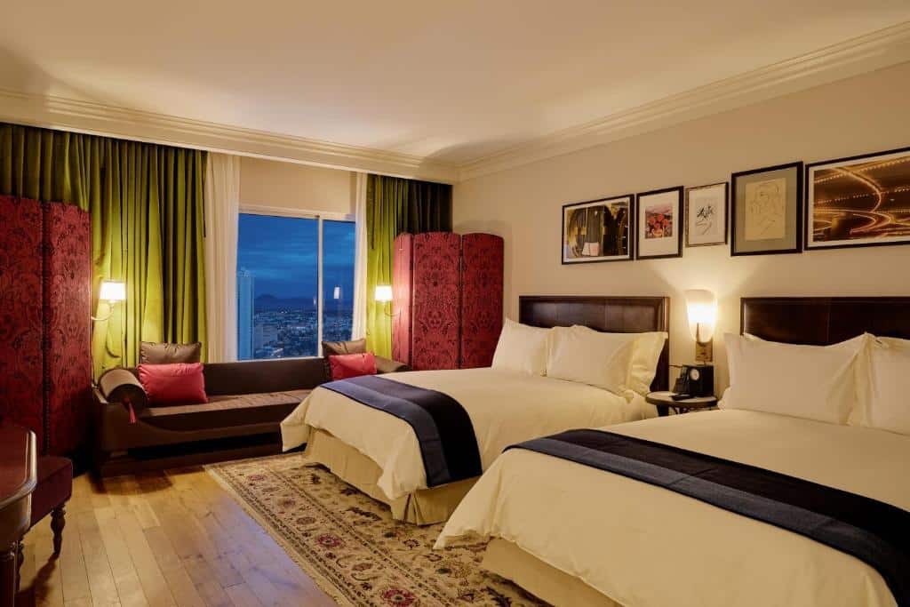 Quarto do Park MGM Las Vegas com duas camas de casal, uma janela ampla com cortinas verdes, e há um sofá pequena em frente da janela, o chão é de madeira clara
