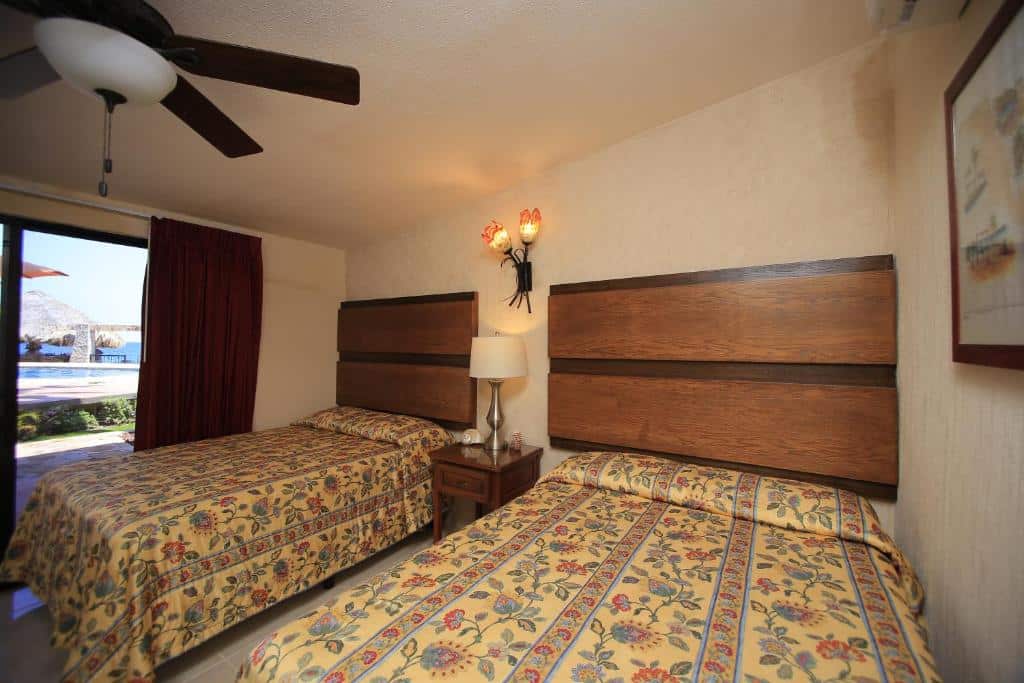 Quarto do Hotel Playa Del Sol com duas camas de solteiro, uma cômoda no meio com luminária e porta de vidro em frente a piscina.