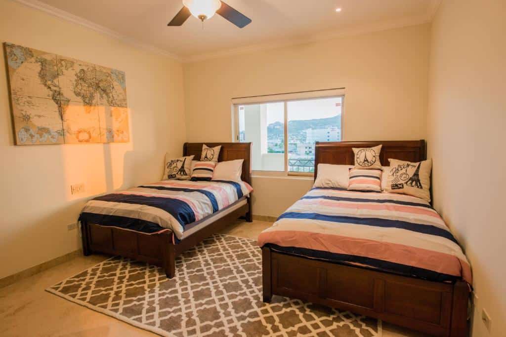 Quarto com duas camas grandes de solteiro do Puerta Cabos Village com janela entre elas, mapa do mapa mundi do lado esquerdo da parede. Representa hotéis em Los Cabos.