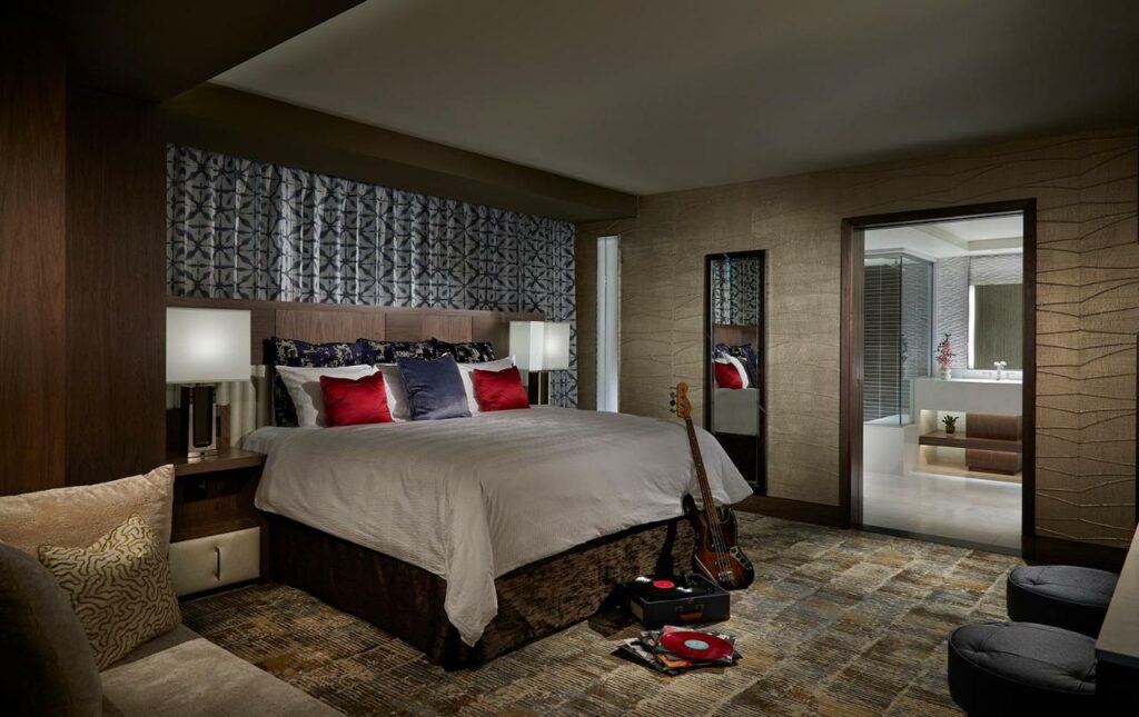 Quarto amplo no Seminole Hard Rock Hotel and Casino Tampa com uma cama de casal, uma sofá, duas poltronas, uma banheiro espaçoso, um peslho e uma cabeceira com dois abajures, a decoração é em branco, vermelho e marrom