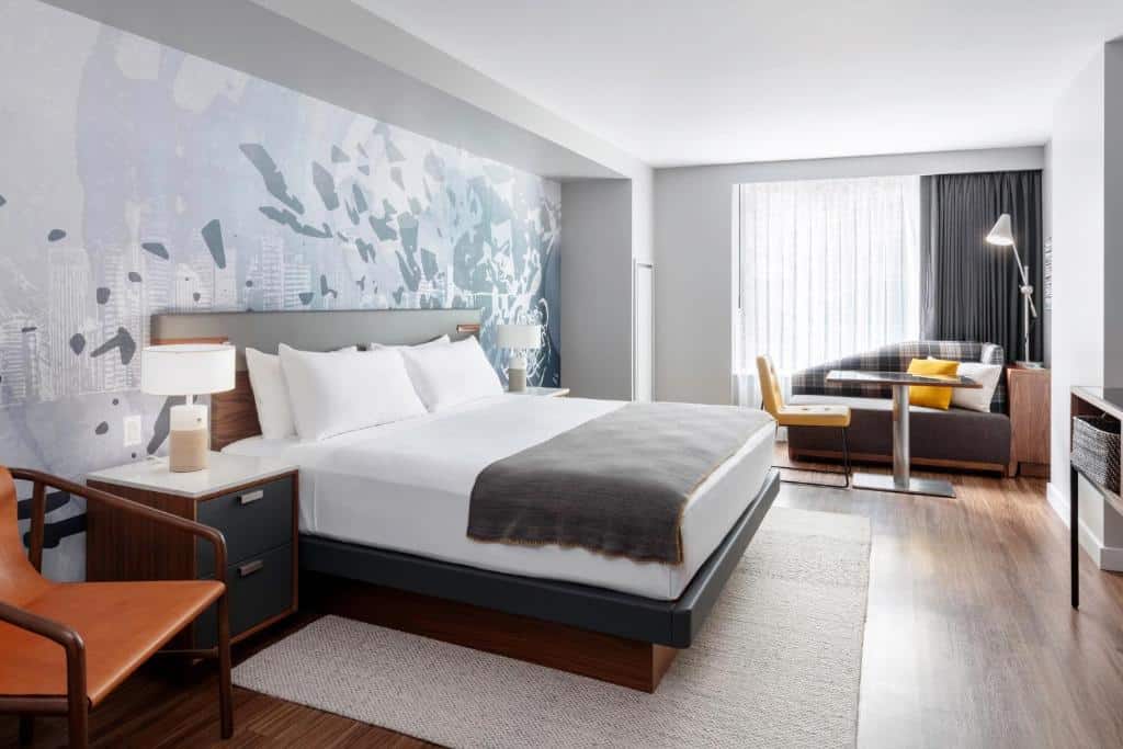 Quarto com cama de casal do The Sound Hotel Seattle Belltown, Tapestry Collection com duas cômodas,com luminárias, mesa de trabalho e sofá.