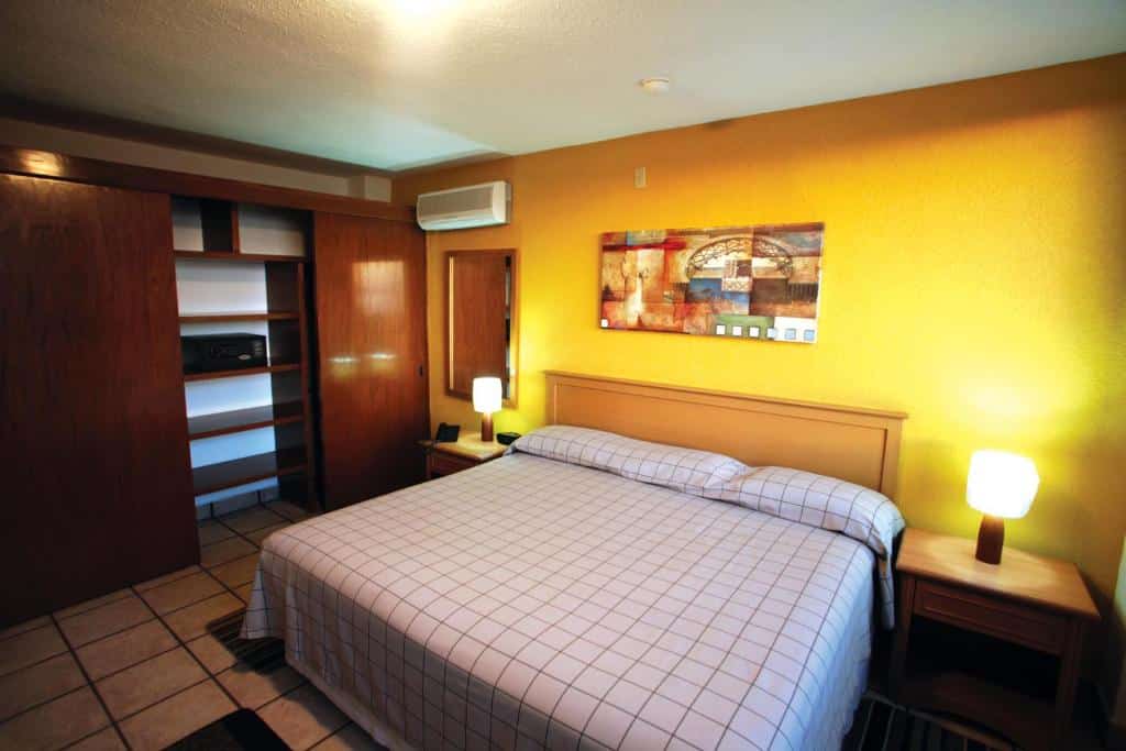 Quarto do Sunrock Condo Hotel com cama de casal, duas cômodas ao lado com luminárias e do lado esquerdo um armário.