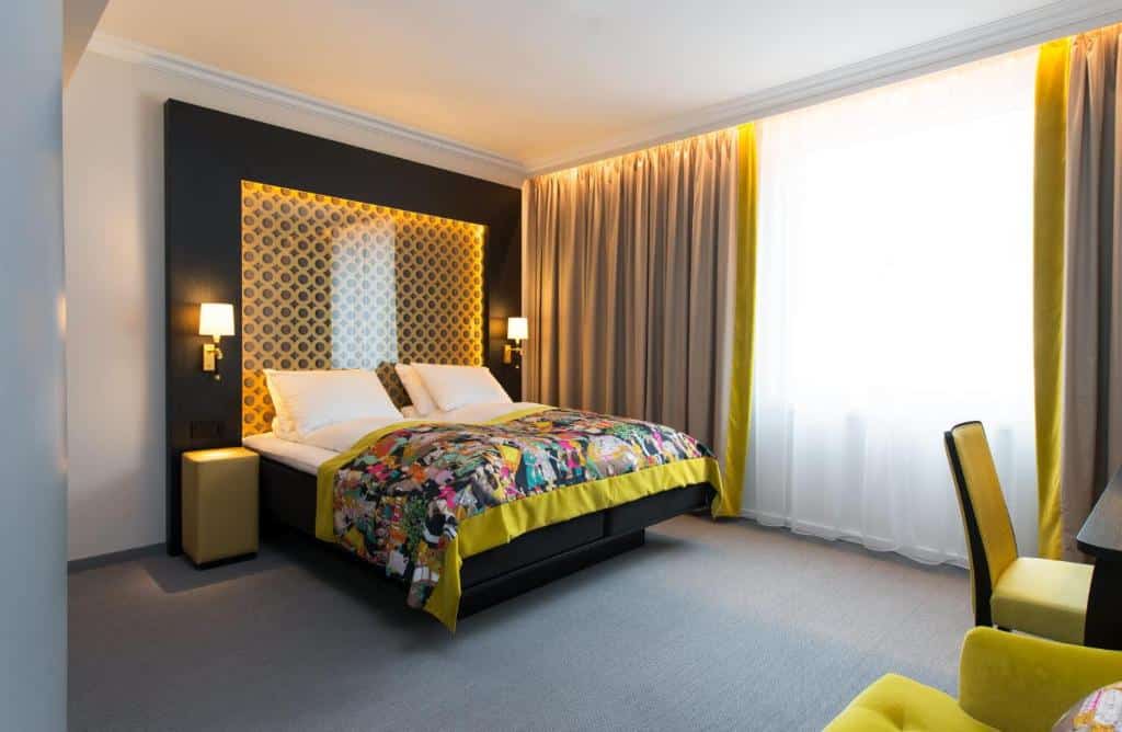 Quarto do Thon Hotel Rosenkrantz Oslo com cama de casal, duas cômodas ao lado da cama com luminárias e a frente da cama uma mesa de trabalho com cadeira.