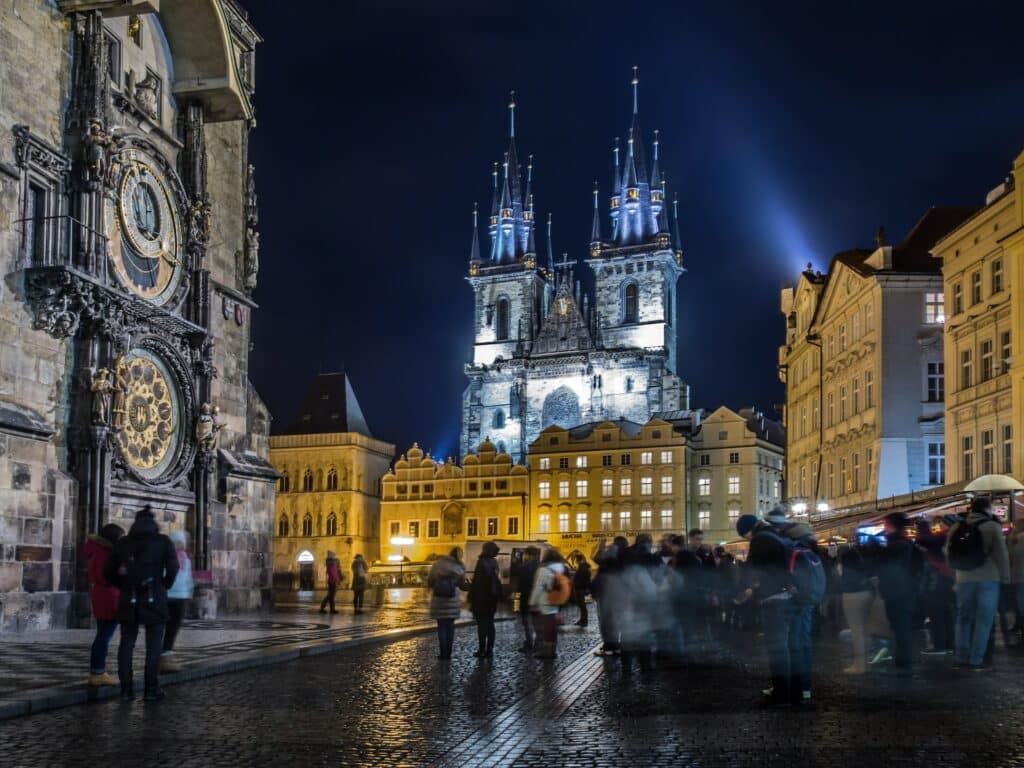 Igreja da Nossa Senhora de Týn, uma categral muito alto em estilo gótico inteira iluminada em uma praça cheia de pessoas em Praga