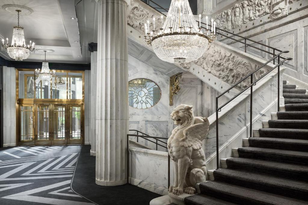 Recepção do The Candler Hotel Atlanta, Curio Collection by Hilton com portas giratórias, escadas e monumento de leão com asas ao pé da escada.