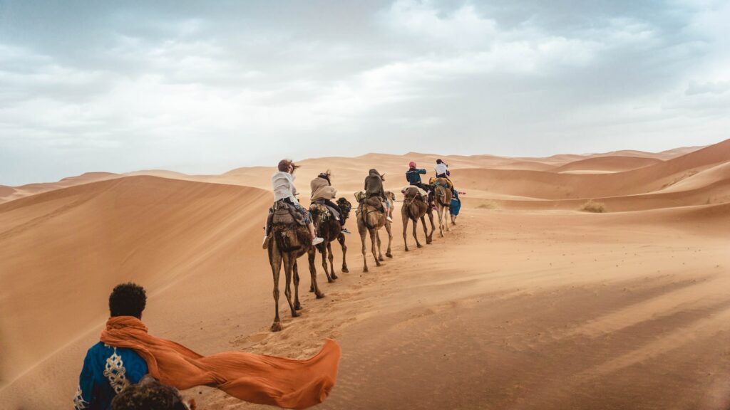 Pessoas andando de camelo no deserto para ilustrar o post seguro viagem Marrakesh. - Foto: Y K via Unsplash