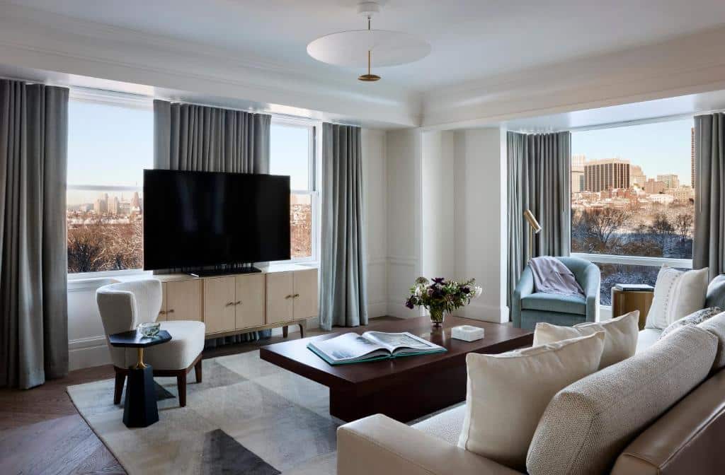 Vista da sala de TV do The Newbury Boston em hotéis em Boston com sofá, TV e mesa de centro.