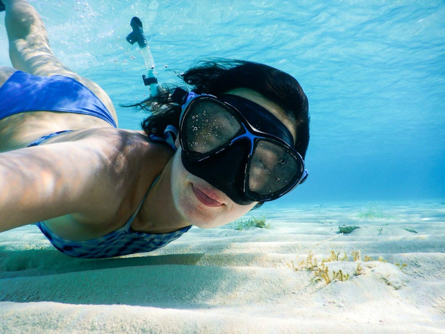 Mulher de biquíni azul tirando selfie embaixo d'água com uma máscara de mergulho no rosto.